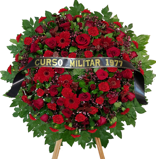 Corona para funeral con gernberas, claveles y rosas rojas, en atril con cinta conmemorativa